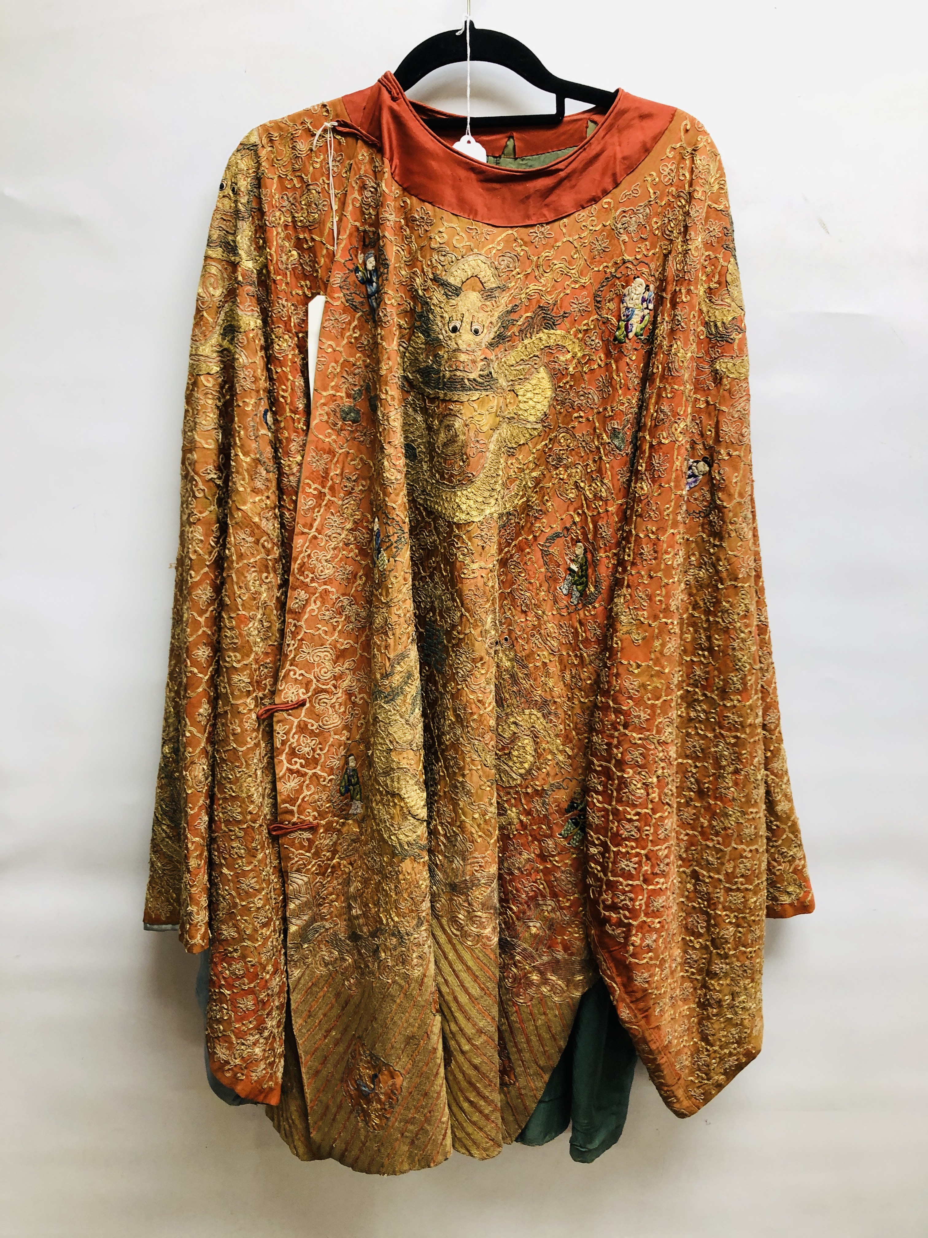 AN ELABORATE ANTIQUE CHINESE SILK CLOAK ON AN ORANGE FIELD EMBROIDERED WITH FIGURES AND GILT