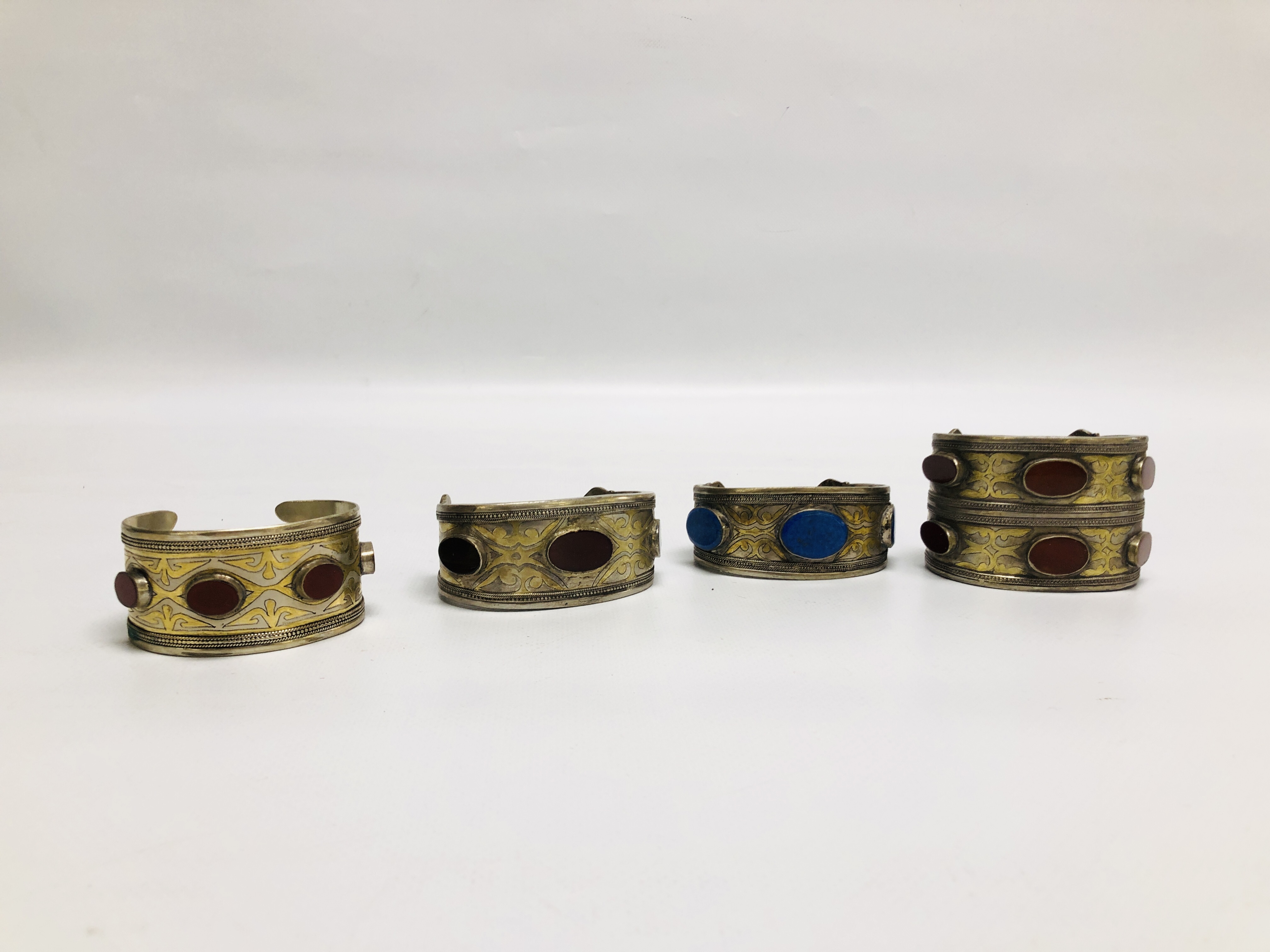 A GROUP OF 4 EASTERN STYLE WHITE METAL CUFF BRACELETS, INSET WITH OVAL STONES.