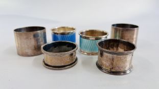 A GROUP OF 6 SILVER SERVIETTE RINGS TO INCLUDE 2 ENAMELLED EXAMPLES.