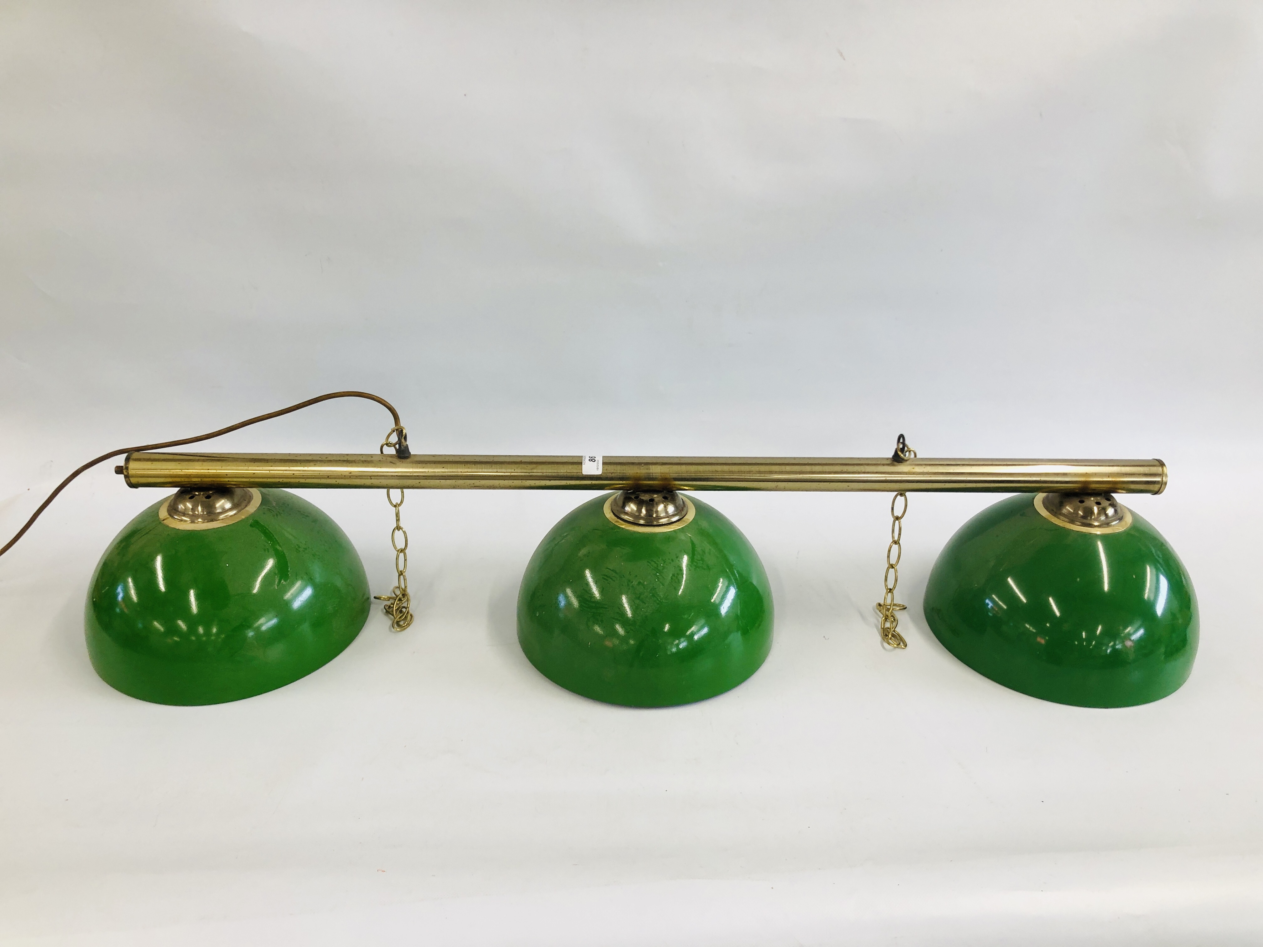 A VINTAGE STYLE CEILING SUSPENDED THREE BULB LIGHT BAR ON BRASS EFFECT TUBE AND GREEN SHADES - SOLD