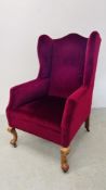 A REPRODUCTION WING BACK FIRE SIDE CHAIR UPHOLSTERED IN BURGUNDY.