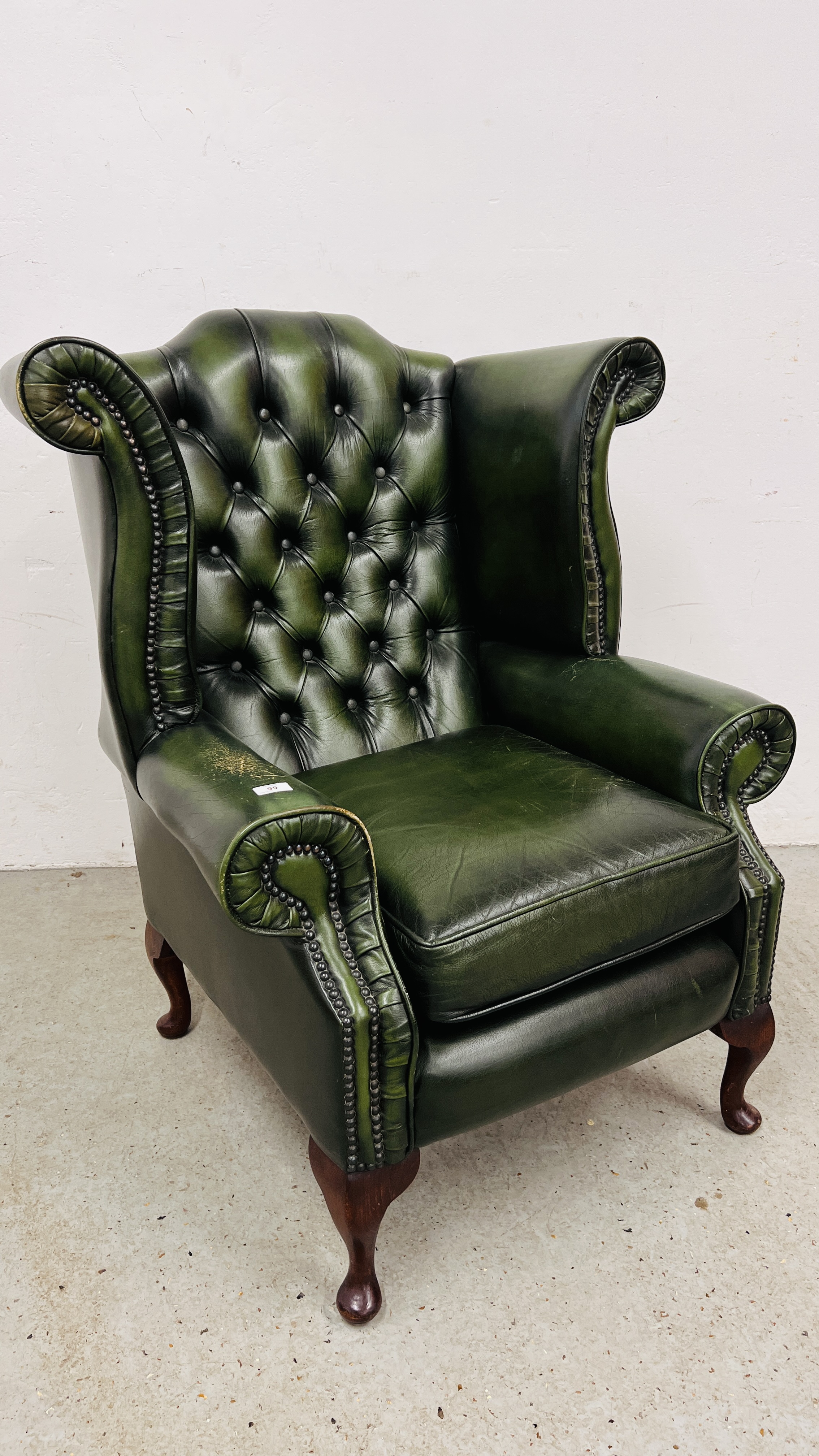 A BOTTLE GREEN LEATHER BUTTON BACK WING CHAIR - FRONT LEG A/F.