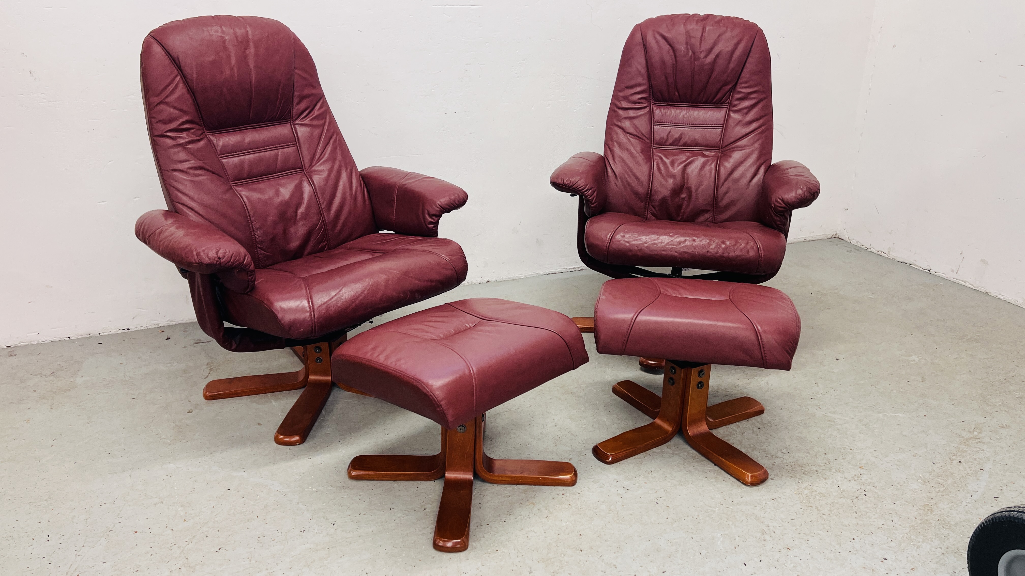 A PAIR OF RED LEATHER REVOLVING ARMCHAIRS WITH FOOTSTOOLS.