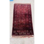 A PERSIAN RUG, THE CENTRAL DESIGN ON A BLACK FIELD, THE FRINGE WITH MULTI-COLOURED RIBBON MOTIFS,