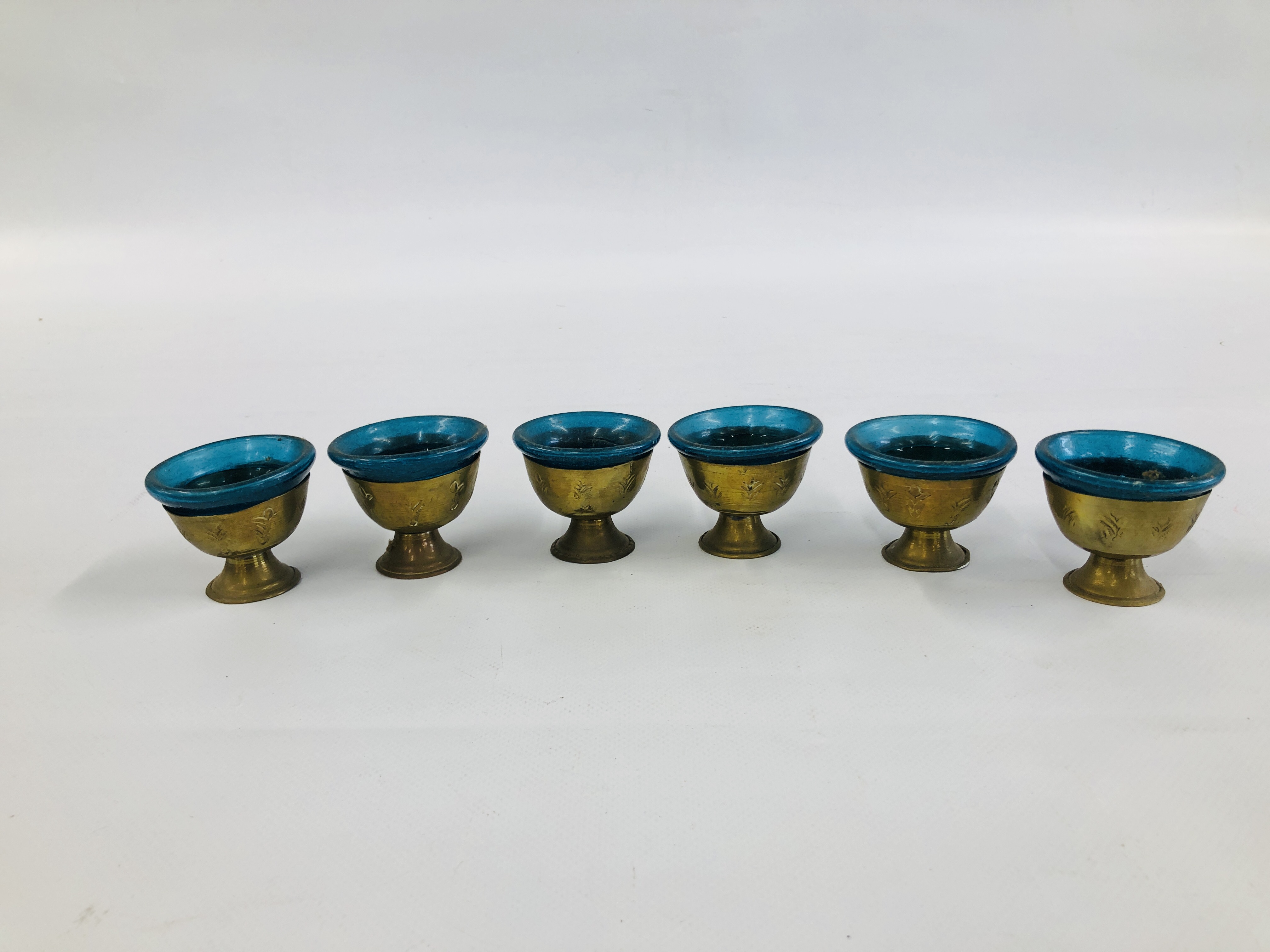 A SET OF SIX MIDDLE EASTERN BRASS GOBLET VESSELS WITH BLUE GLASS LINERS.