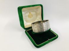A VINTAGE WHITE METAL ENGRAVED HINGED BANGLE IN AN ANTIQUE GREEN VELVET BOX MARKED "THE ALEX CLARK"