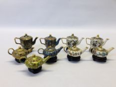 A COLLECTION OF 9 MINIATURE ORIENTAL ENAMELLED TEAPOTS ON CARVED HARDWOOD STANDS.