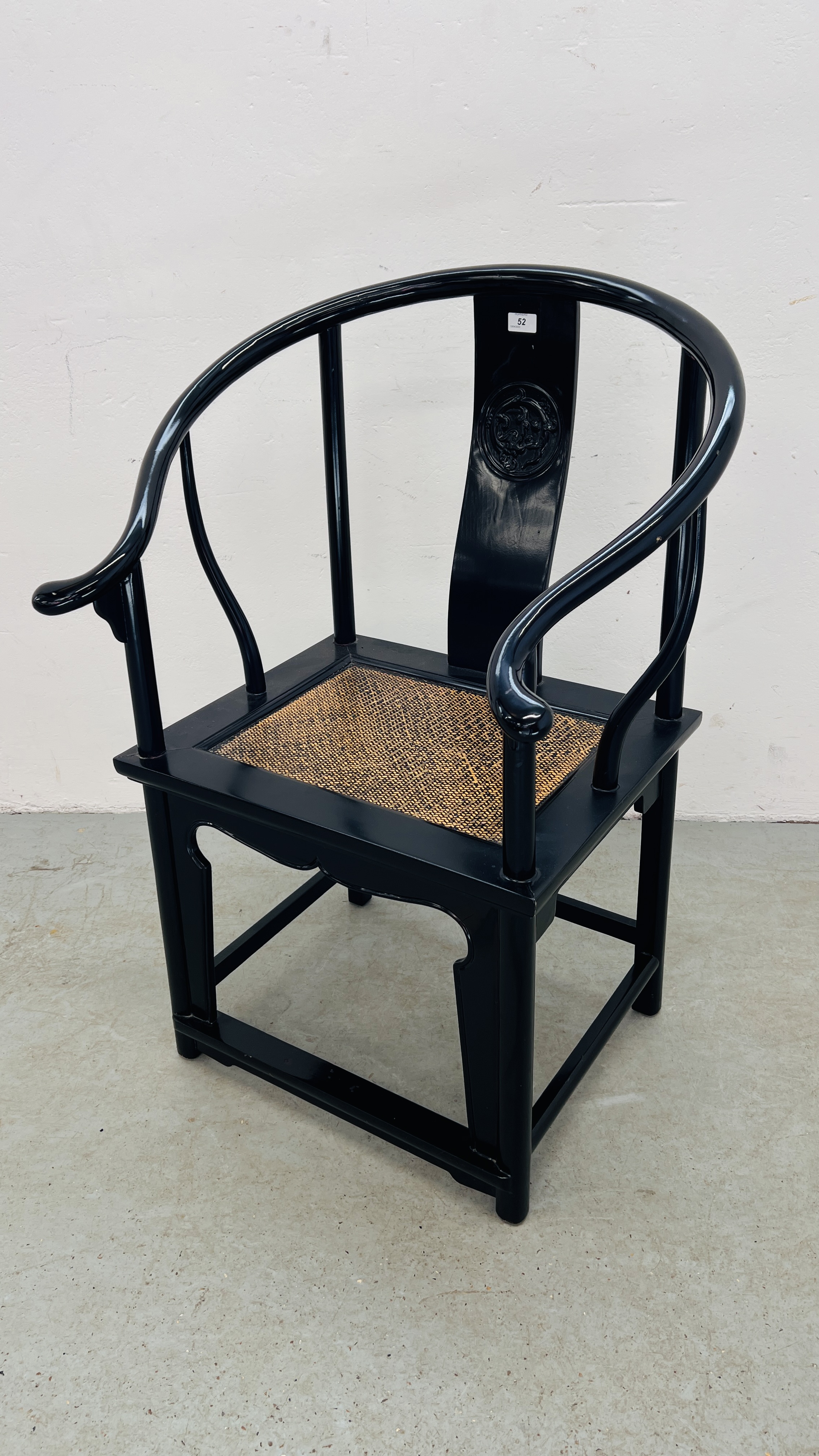 AN ORIENTAL BLACK LACQUERED ARM CHAIR WITH CARVED SYMBOL TO REAR SUPPORT.
