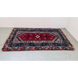 A TRADITIONAL ORIENTAL RUG WITH CENTRAL HOOKED MOTIF ON A BLUE POLE,