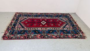 A TRADITIONAL ORIENTAL RUG WITH CENTRAL HOOKED MOTIF ON A BLUE POLE,