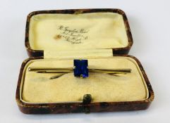 A 9CT GOLD BAR BROOCH SET WITH BAGUETTE BLUE STONE IN VINTAGE PRESENTATION BOX.