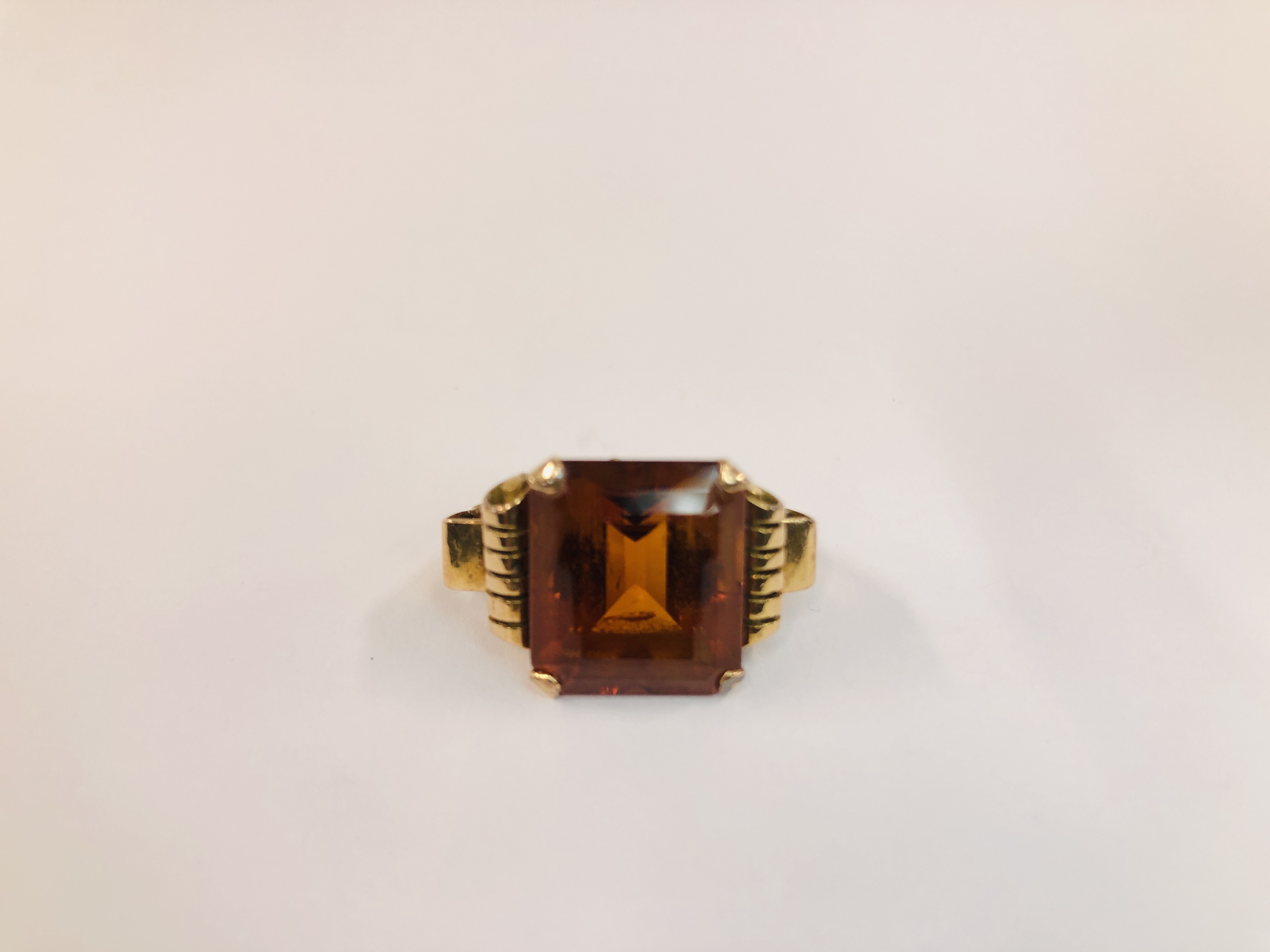 AN UNMARKED YELLOW METAL RING SET WITH AN EMERALD CUT AMBER COLOURED STONE H 1.4CM X W 1.4CM.