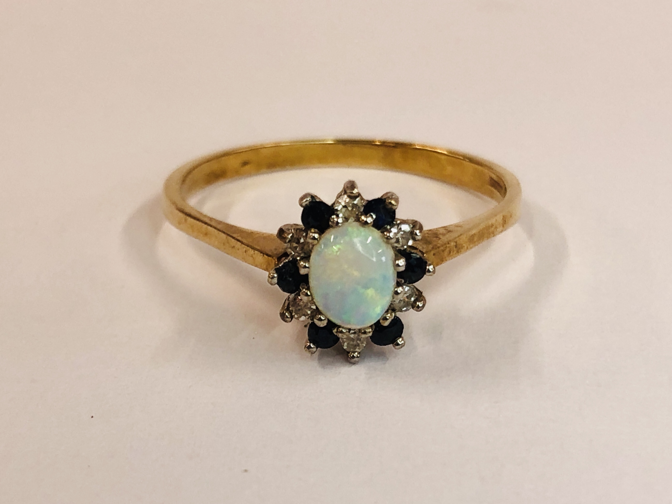 A 9CT GOLD RING SET WITH CENTRAL OVAL OPAL, SURROUNDED BY SMALLER DIAMONDS AND SAPPHIRES.
