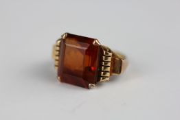 AN UNMARKED YELLOW METAL RING SET WITH AN EMERALD CUT AMBER COLOURED STONE H 1.4CM X W 1.4CM.