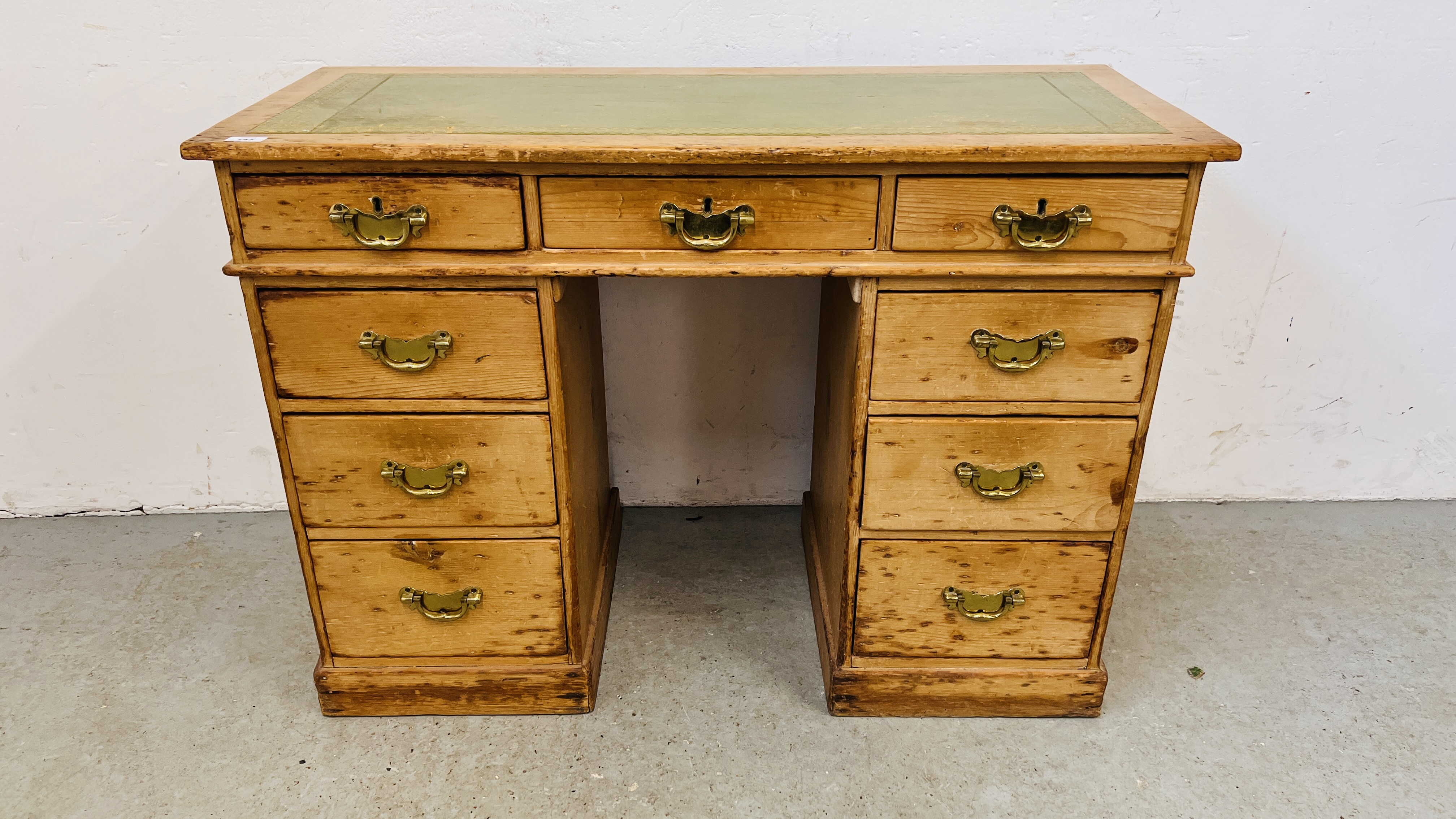 AN ANTIQUE WAXED PINE NINE DRAWER KNEEHOLE DESK WITH TOOLED LEATHER INSET TOP.