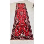 A RED PATTERNED EASTERN HALL RUNNER, 305CM X 77CM.