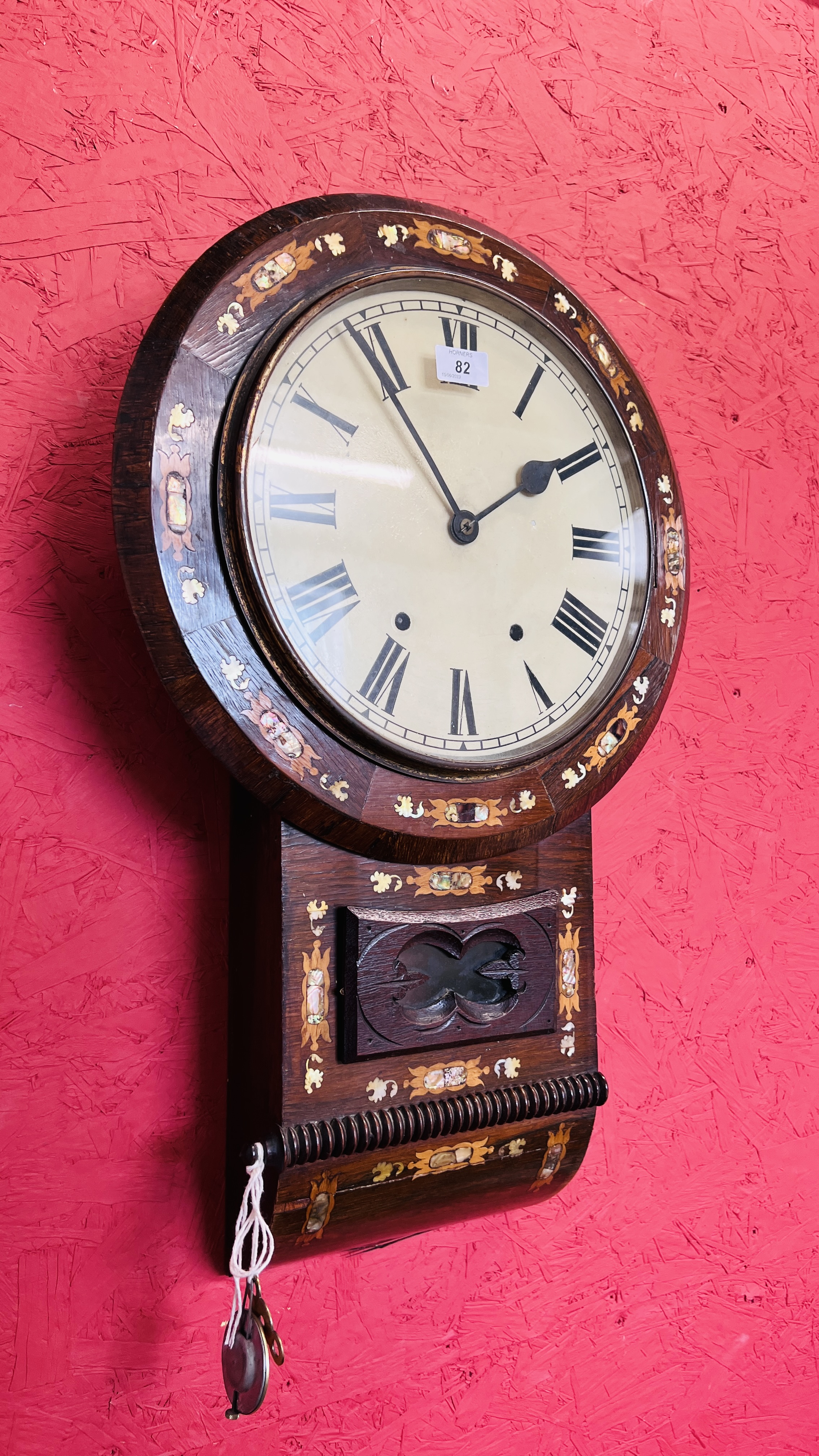 AN ANTIQUE GINGERBREAD STYLE MAHOGANY WALL CLOCK WITH MOTHER OF PEARL INLAY.