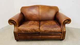 A TAN LEATHER TWO SEATER SOFA WITH WORN PATINA.