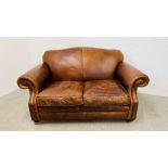 A TAN LEATHER TWO SEATER SOFA WITH WORN PATINA.