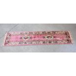 A MACHINE MADE WOOL HALL RUNNER CARPET ON PINK BACKGROUND.