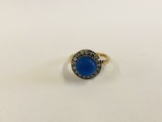 AN 18CT GOLD RING SET WITH CENTRAL BLUE STONE, SURROUNDED BY SMALLER DIAMOND IN A HALO SETTING.