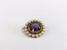 AN ANTIQUE YELLOW METAL BROOCH SET WITH CENTRAL AMETHYST SURROUNDED BY SMALLER PEARLS.