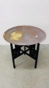 AN ORIENTAL BRASS TRAY TOP TABLE WITH FOLDING CARVED WOODEN BASE - DIA 64CM.