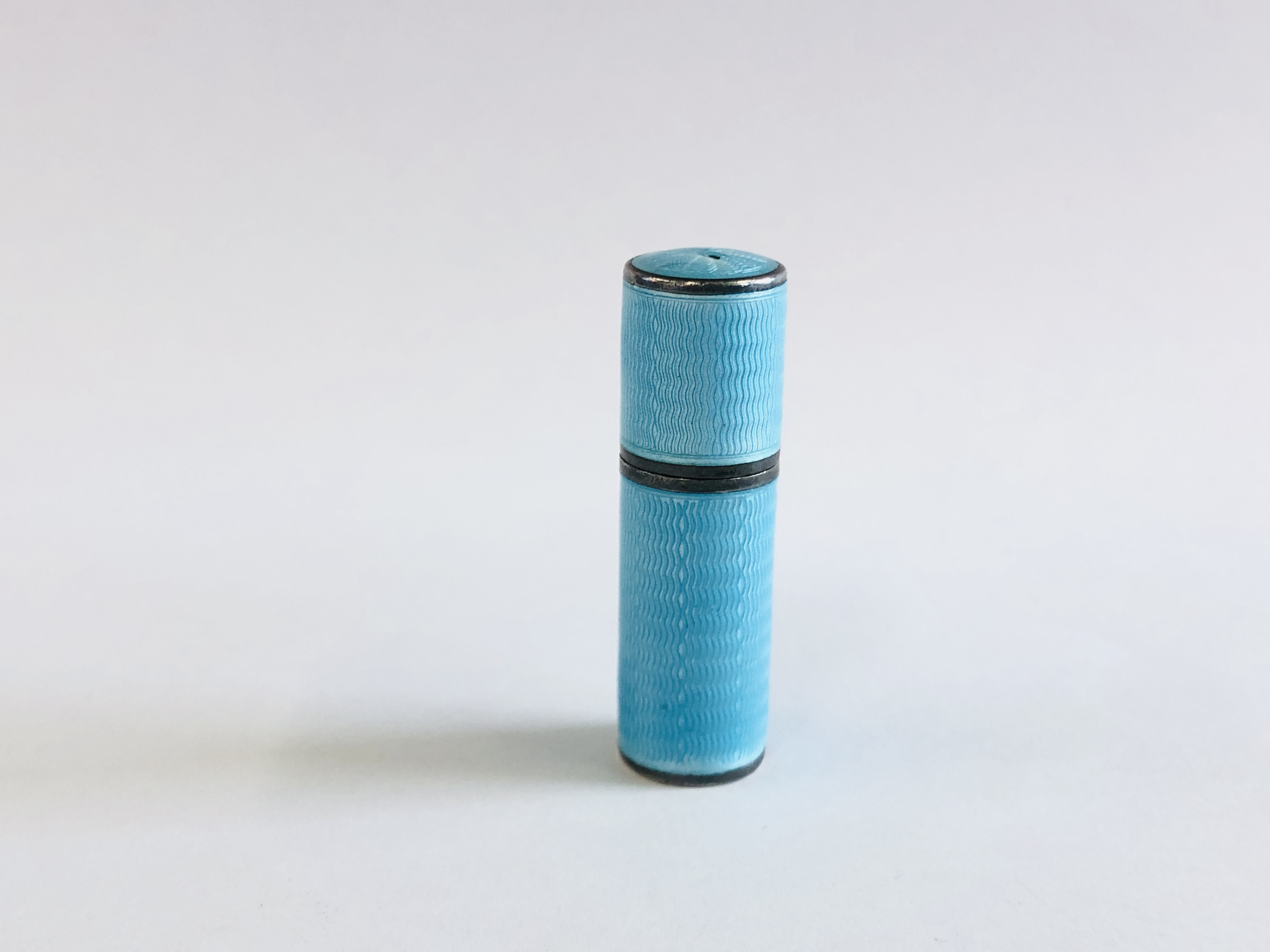 A VINTAGE ENAMELED SILVER CYLINDRICAL THREADED SCENT BOTTLE HOLDER CONTAINING A CLEAR GLASS SCENT