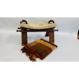 A VINTAGE STYLE CAMEL SADDLE FOOTSTOOL AND TASSELED THROW.