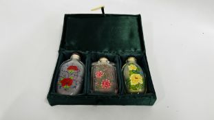 A CASED SET OF THREE ORIENTAL GLASS PERFUME BOTTLES DECORATED WITH VARIOUS BLOSSOM IN A FITTED CASE.