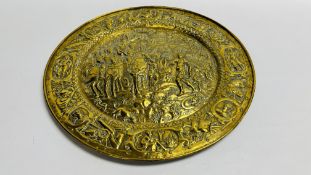 A LARGE BRASS EMBOSSED CHARGER DEPICTING GRECIAN MEN ON HORSE BACK 56.5CM DIAMETER.