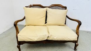 ANTIQUE OAK TWO SEATER SOFA WITH WICKER AND CARVED BACK PANEL SUPPORTS, WITH CREAM CUSHIONS.