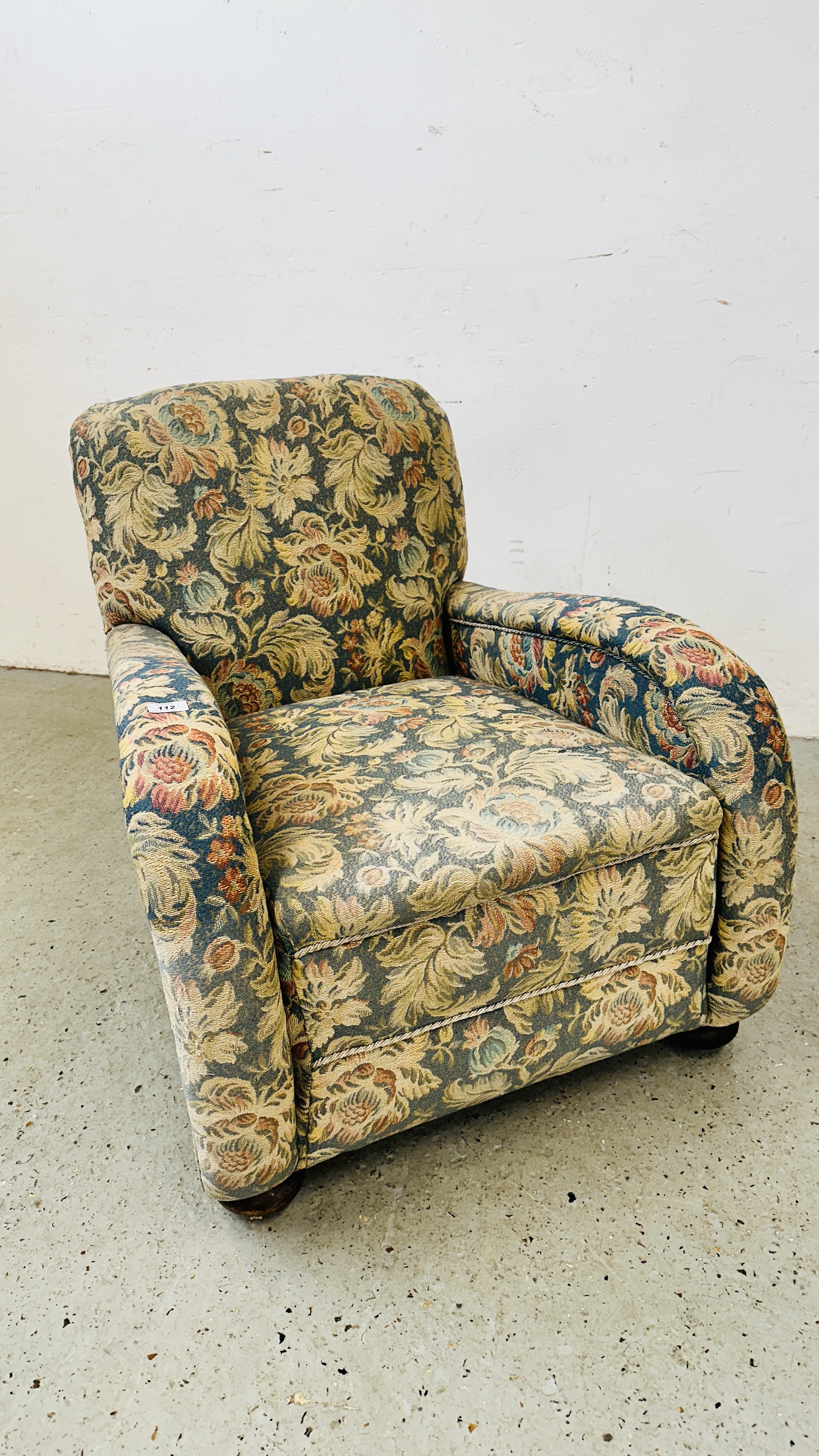 AN ANTIQUE EASY ARMCHAIR ON BUN FEET IN FLORAL UPHOLSTERY.