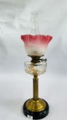 A BRASS COLUMNED OIL LAMP WITH PINK FROSTED SHADE.