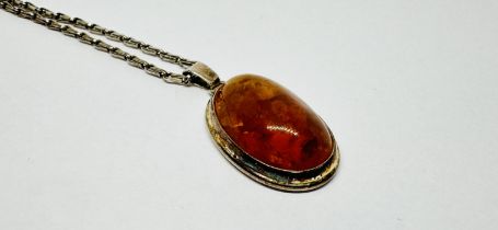 A SILVER MOUNTED OVAL AMBER PENDANT ON A WHITE METAL CHAIN, L 50CM.