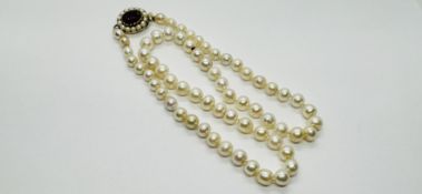 A SINGLE STRAND NECKLACE OF PEARLS, THE YELLOW CLASP SET WITH A RED STONE - LENGTH 45.5CM.