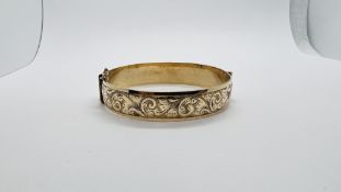 A ROLLED GOLD HINGED BANGLE WITH CHASED DECORATION AND SAFETY CHAIN.