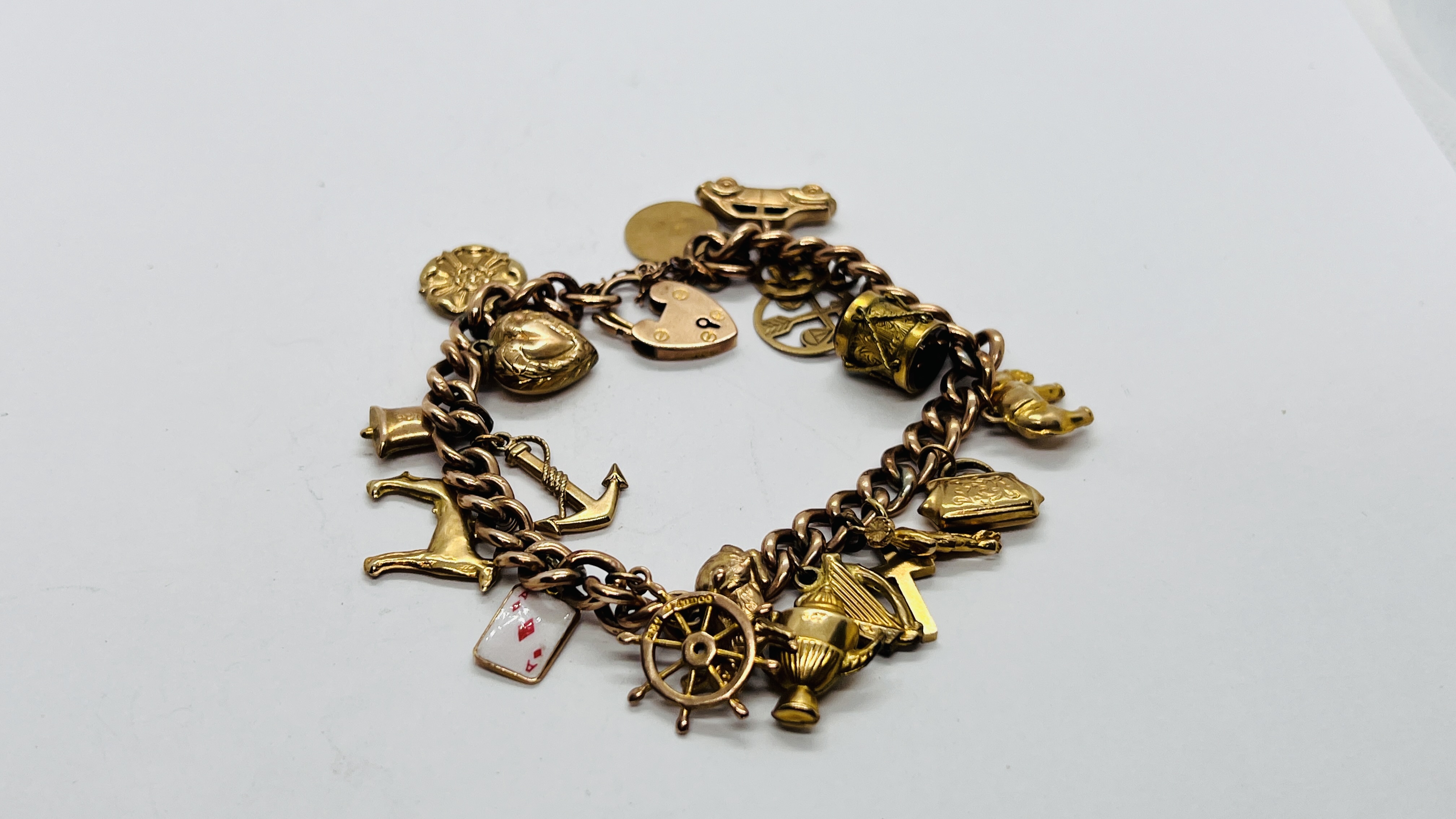 A 9CT GOLD CHARM BRACELET WITH SAFETY CHAIN AND PADLOCK CLASP ALONG WITH 18 9CT CHARMS AND A