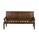 AN 18TH CENTURY JOINED OAK SETTLE WITH PANELLED BACK AND SCROLLED SIDE ARMS ON TAPERING LEGS