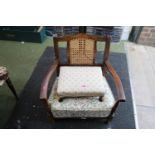 1930s Low upholstered cane backed elbow chair and a upholstered footstool with squat paw feet