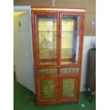 A oriental style lacquer display cabinet with two glazed doors, drawers and cupboards under