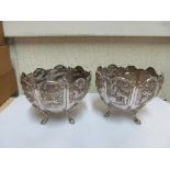 A pair metal oriental bowls on paw feet one embossed exotic animals the other figures