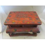An oriental red lacquer low table scenes of figures amongst buildings and flowers