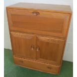 An Ercol Golden Dawn cabinet with drop down front above two cupboard doors and drawer