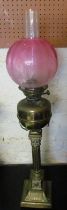 A brass oil lamp on column base with pink glass shade