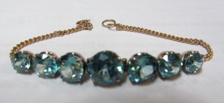 A gold coloured bracelet with seven blue Zircon stones