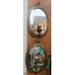 A pair of oval brass mirrors with bow cresting and candle sconce