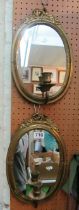 A pair of oval brass mirrors with bow cresting and candle sconce