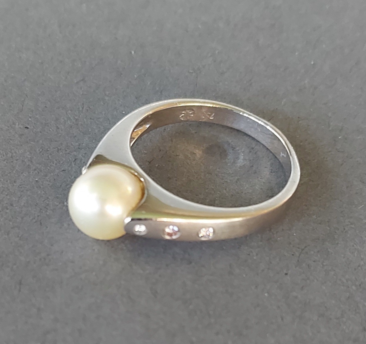 An 18ct white gold ring set with a central pearl flanked by diamond shoulders, 6.5gms