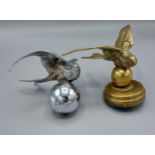 A brass car mascot in the form of a bird together with another similar